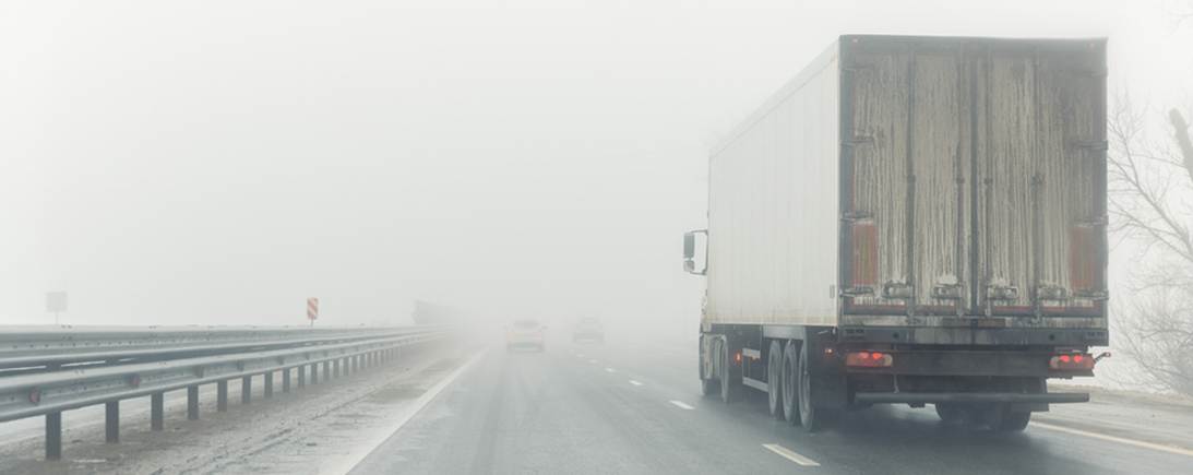 A truck driving on a highway surrounded by heavy fog. 